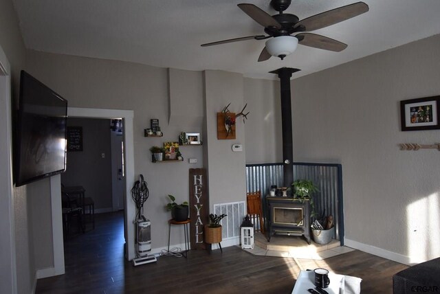 living room featuring dark hardwood / wood-style floors, ceiling fan, and a wood stove