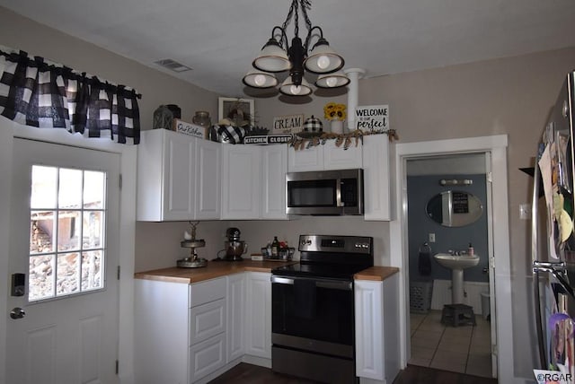 kitchen featuring pendant lighting, wood counters, white cabinets, stainless steel appliances, and an inviting chandelier