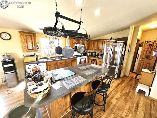 kitchen featuring freestanding refrigerator, white range with gas cooktop, light wood-style floors, brown cabinetry, and vaulted ceiling