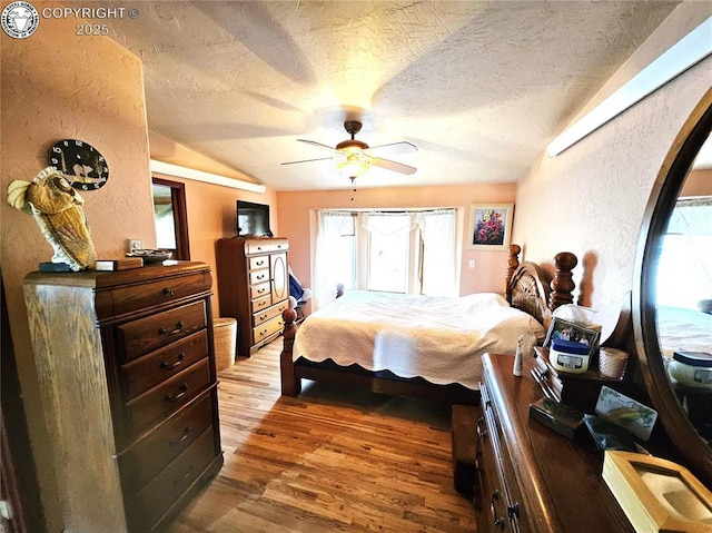 bedroom with wood finished floors, a textured wall, a textured ceiling, vaulted ceiling, and a ceiling fan