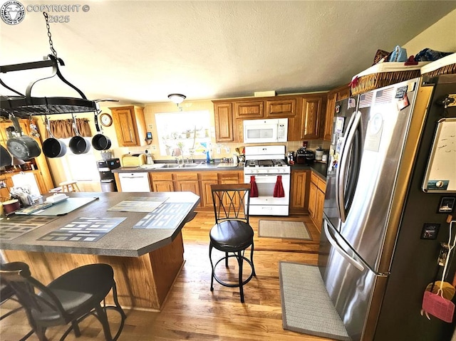kitchen with white appliances, dark countertops, light wood-style floors, a breakfast bar, and a textured ceiling