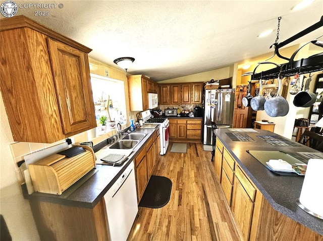 kitchen featuring white appliances, a sink, light wood-style floors, vaulted ceiling, and brown cabinetry