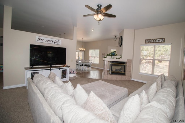 carpeted living room featuring ceiling fan with notable chandelier, a tile fireplace, and a healthy amount of sunlight