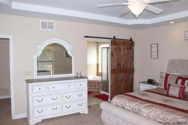 bedroom featuring ceiling fan, connected bathroom, a barn door, light carpet, and a raised ceiling