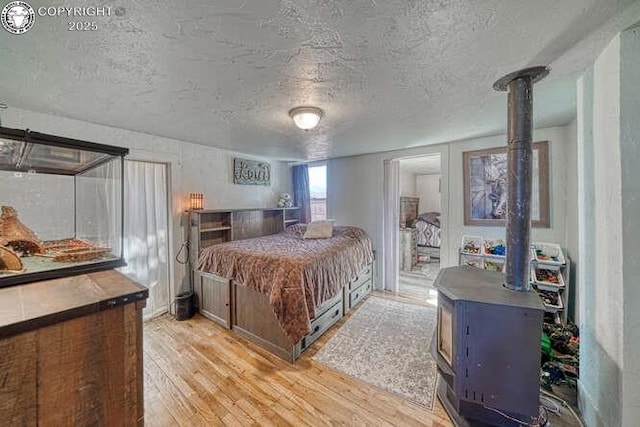 bedroom featuring a textured ceiling, light wood-style flooring, and a wood stove