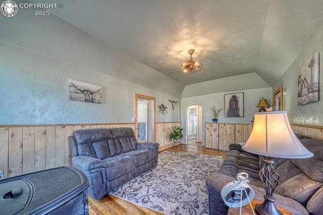 living area featuring arched walkways, wainscoting, vaulted ceiling, and wood finished floors