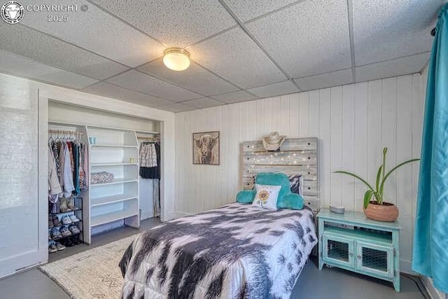 bedroom with concrete flooring, a closet, and a drop ceiling