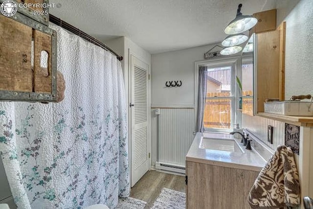 full bath featuring a baseboard radiator, wood finished floors, a textured ceiling, and wainscoting