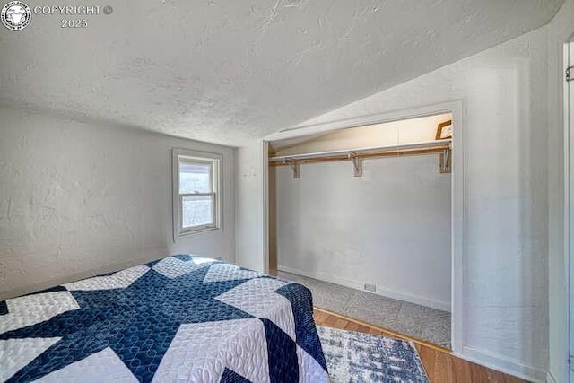 bedroom featuring a closet, a textured wall, vaulted ceiling, a textured ceiling, and wood finished floors