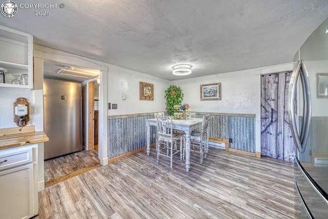 dining space featuring light wood-type flooring, a wainscoted wall, and a textured ceiling