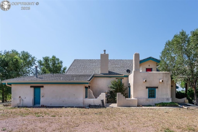 rear view of house with stucco siding, a tiled roof, and a chimney