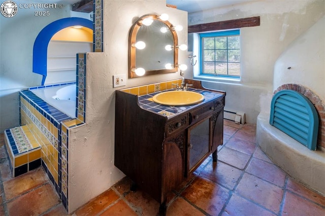 full bathroom featuring vanity, stone tile flooring, tiled bath, and a baseboard radiator