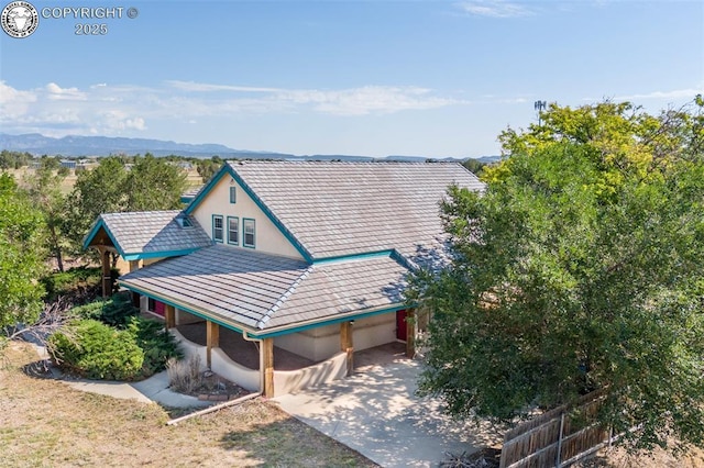 exterior space featuring stucco siding, a tile roof, fence, a mountain view, and concrete driveway