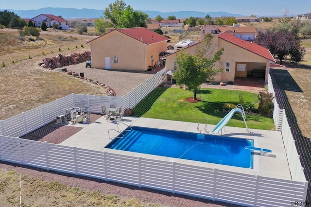 view of swimming pool featuring a patio area, a water slide, a diving board, a yard, and a mountain view