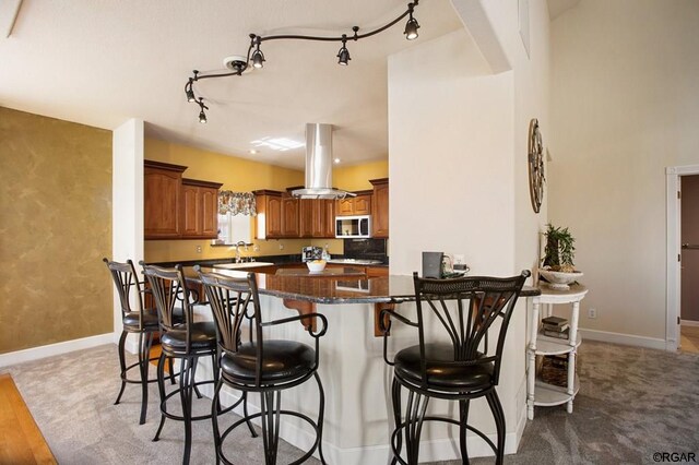 kitchen featuring sink, a breakfast bar area, island range hood, dark stone countertops, and kitchen peninsula