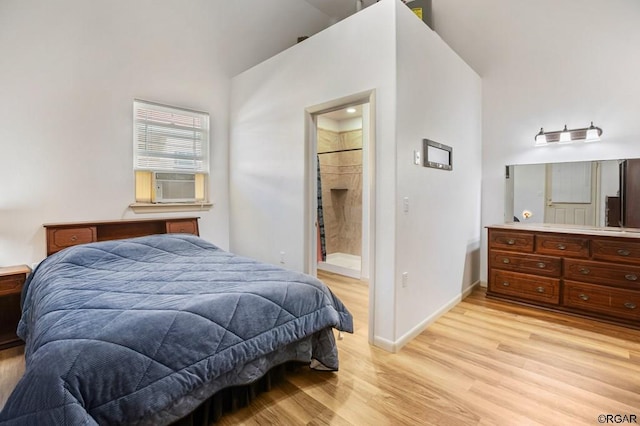 bedroom with cooling unit, a towering ceiling, connected bathroom, and light wood-type flooring