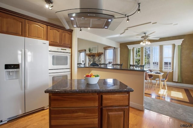 kitchen with dark stone countertops, a center island, ceiling fan, light hardwood / wood-style floors, and white appliances