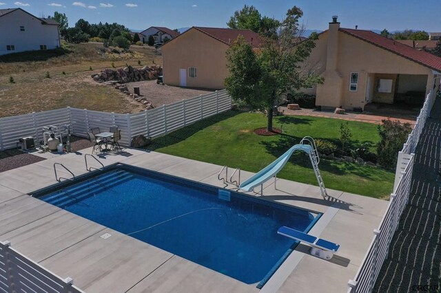 view of pool with a water slide, a diving board, a patio area, and a lawn