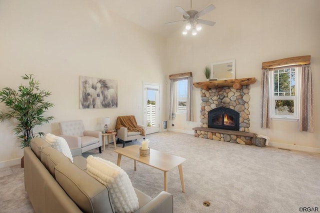 living room with a high ceiling, a stone fireplace, light colored carpet, and ceiling fan