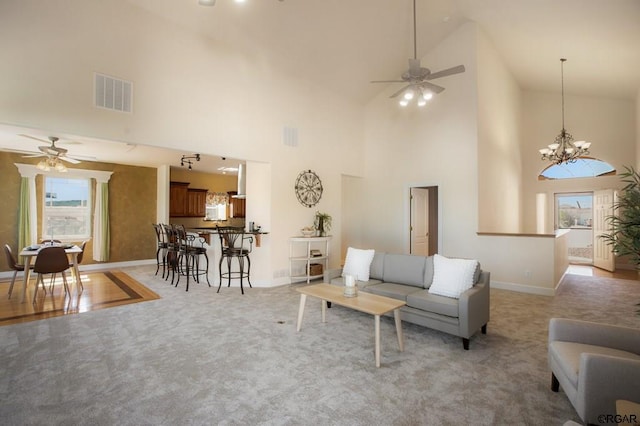 carpeted living room featuring ceiling fan with notable chandelier and high vaulted ceiling