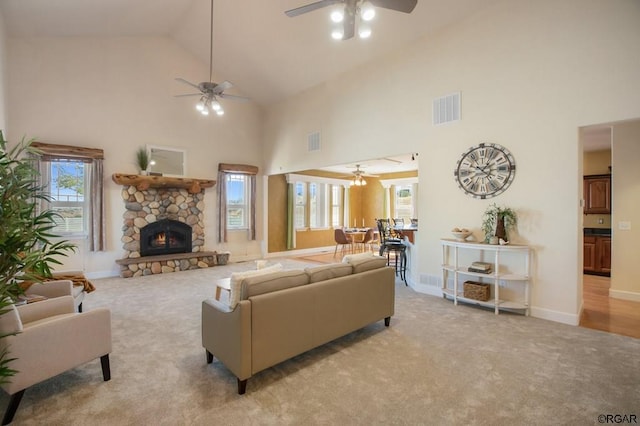 carpeted living room with a stone fireplace, high vaulted ceiling, and ceiling fan