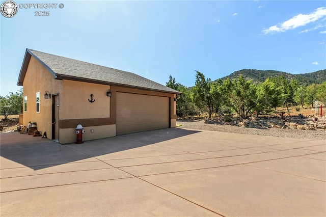 view of home's exterior with a shingled roof, a mountain view, a garage, and stucco siding