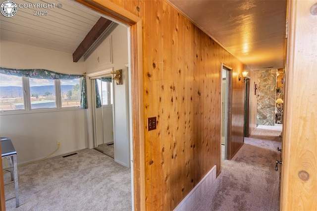 hall with wooden ceiling, wooden walls, light carpet, and vaulted ceiling with beams