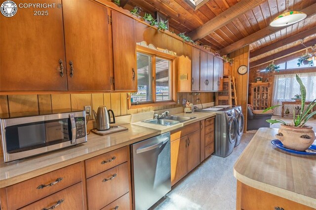 kitchen with appliances with stainless steel finishes, wood walls, sink, wooden ceiling, and washer and clothes dryer