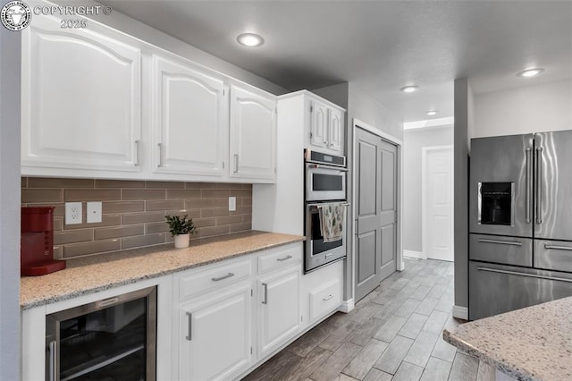 717 Tyrolean Way, Canon City, CO 81212 - kitchen featuring appliances with stainless steel finishes, beverage cooler, backsplash, white cabinetry, and light stone countertops