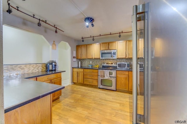 kitchen featuring stainless steel appliances, kitchen peninsula, light hardwood / wood-style floors, and decorative backsplash