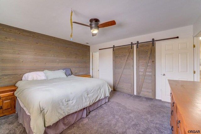 bedroom with a barn door, ceiling fan, carpet, and wooden walls