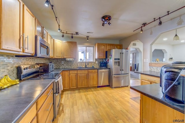 kitchen featuring sink, backsplash, stainless steel appliances, light hardwood / wood-style floors, and decorative light fixtures