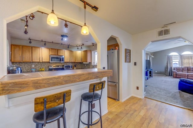 kitchen featuring appliances with stainless steel finishes, decorative light fixtures, a breakfast bar area, backsplash, and kitchen peninsula