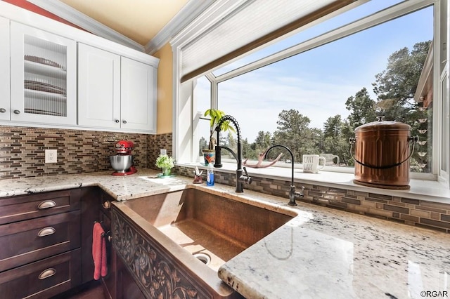 kitchen with sink, dark brown cabinets, white cabinets, light stone countertops, and backsplash