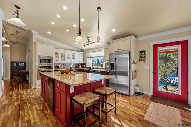 kitchen with a breakfast bar area, appliances with stainless steel finishes, white cabinetry, a center island, and decorative light fixtures