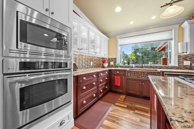 kitchen with sink, stainless steel appliances, tasteful backsplash, light stone countertops, and light hardwood / wood-style floors