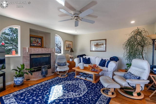 living room featuring hardwood / wood-style flooring, a tiled fireplace, and ceiling fan