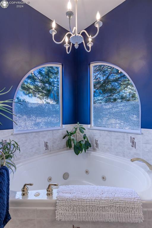 bathroom with tiled tub and a chandelier