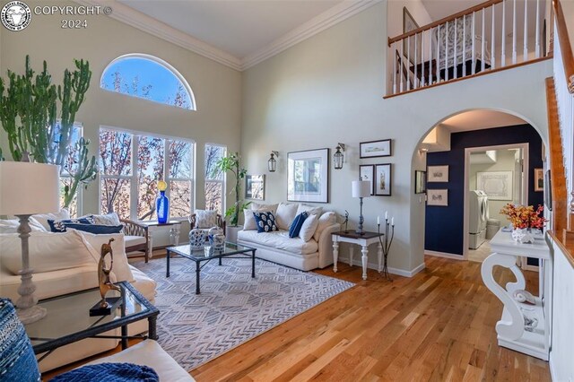 living room with ornamental molding, light hardwood / wood-style floors, independent washer and dryer, and a high ceiling