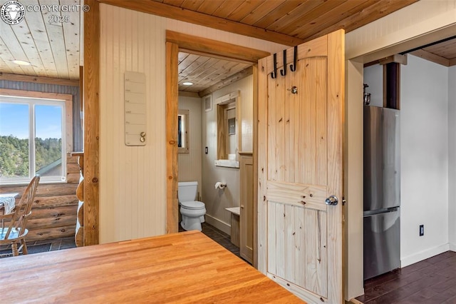 bathroom featuring wood finished floors, baseboards, wooden ceiling, toilet, and rustic walls