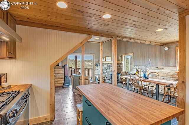 kitchen with tile patterned flooring, wooden counters, stainless steel range with gas cooktop, wall chimney range hood, and lofted ceiling