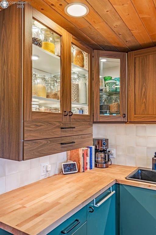 kitchen with blue cabinets, wood counters, backsplash, wooden ceiling, and glass insert cabinets