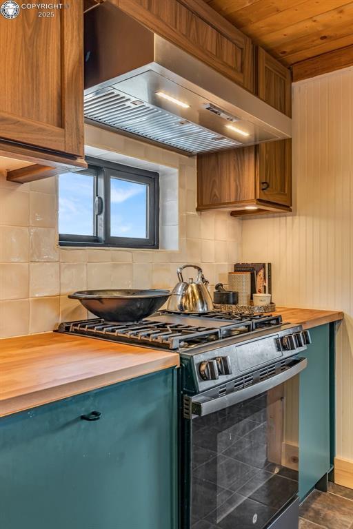 kitchen with gas stove, butcher block countertops, wood ceiling, wall chimney exhaust hood, and backsplash