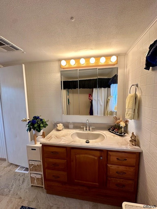 bathroom with vanity, a textured ceiling, and tile walls