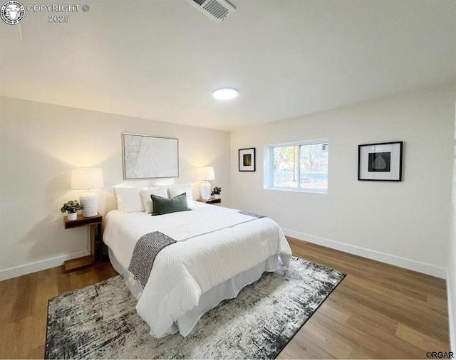 bedroom with baseboards, visible vents, and wood finished floors