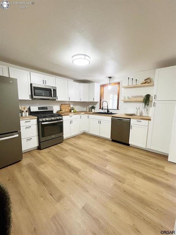 kitchen featuring appliances with stainless steel finishes, a sink, white cabinetry, and light wood-style floors