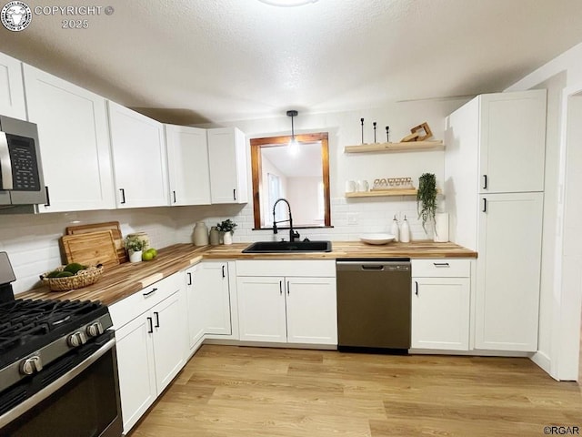 kitchen with appliances with stainless steel finishes, light wood-style floors, a sink, and wood counters