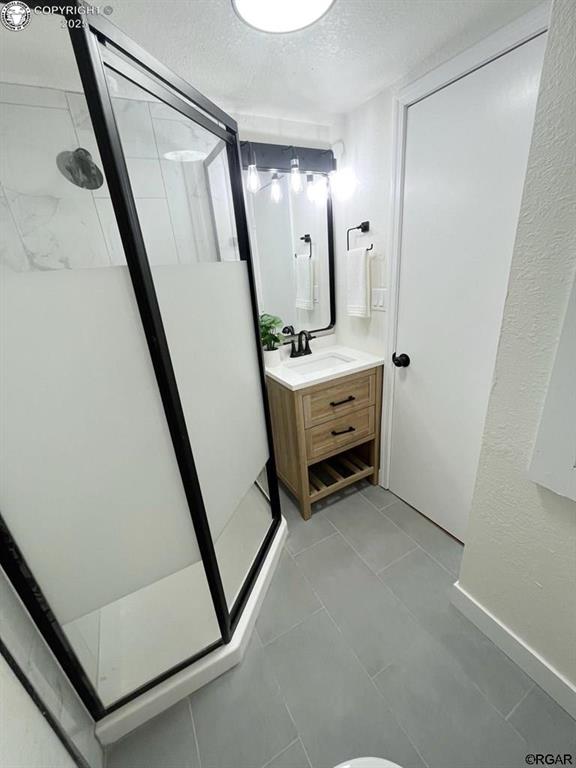 full bathroom with tile patterned flooring, a shower stall, a textured ceiling, and vanity