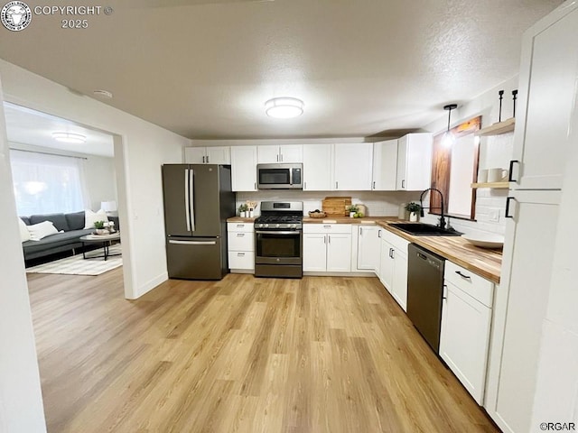 kitchen with appliances with stainless steel finishes, light wood-style floors, white cabinetry, a sink, and butcher block countertops