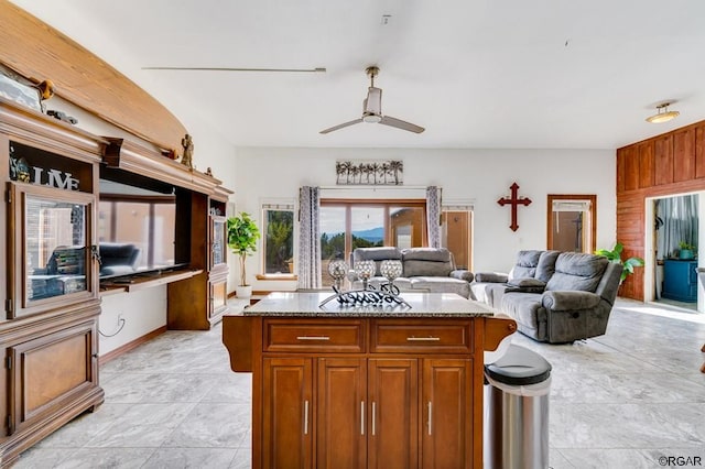 kitchen with ceiling fan, a center island, light stone counters, and wooden walls